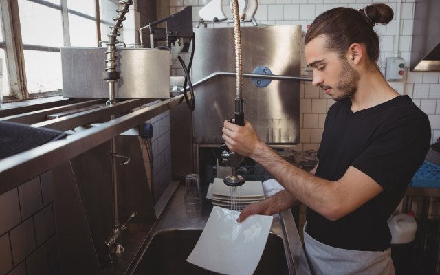 A man washes plates in a professional kitchen