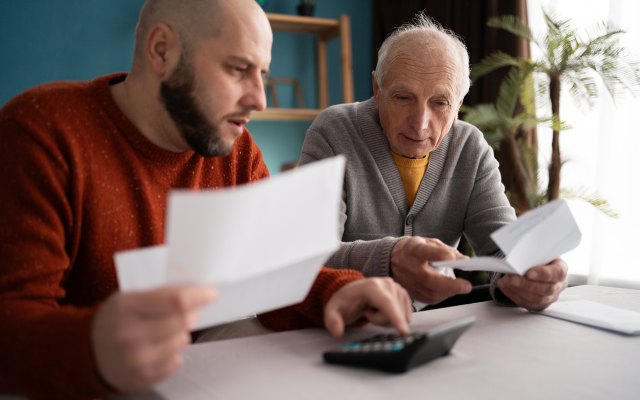 An older man and younger man discuss paper documents