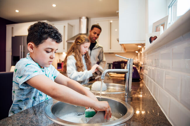 Children and an adult at the kitchen sink washing up dishes