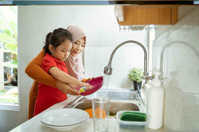 A woman and child washing up together in the kitchen