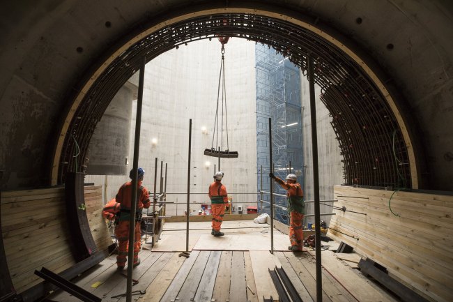 Three works inside a giant new sewer watching a crane